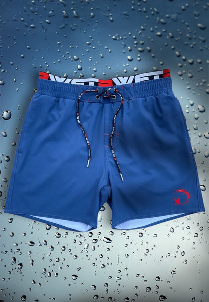 Displayed against a backdrop of water droplets, the Be Extraordinary at the Beach with Infinity Beach Shorts by BWET Swimwear combine eco-friendliness with style. These blue swim trunks feature a distinctive red fish logo on the left leg, a drawstring waistband accented in red and white, and an inner lining crafted from recycled materials showcasing a striking black and red design.