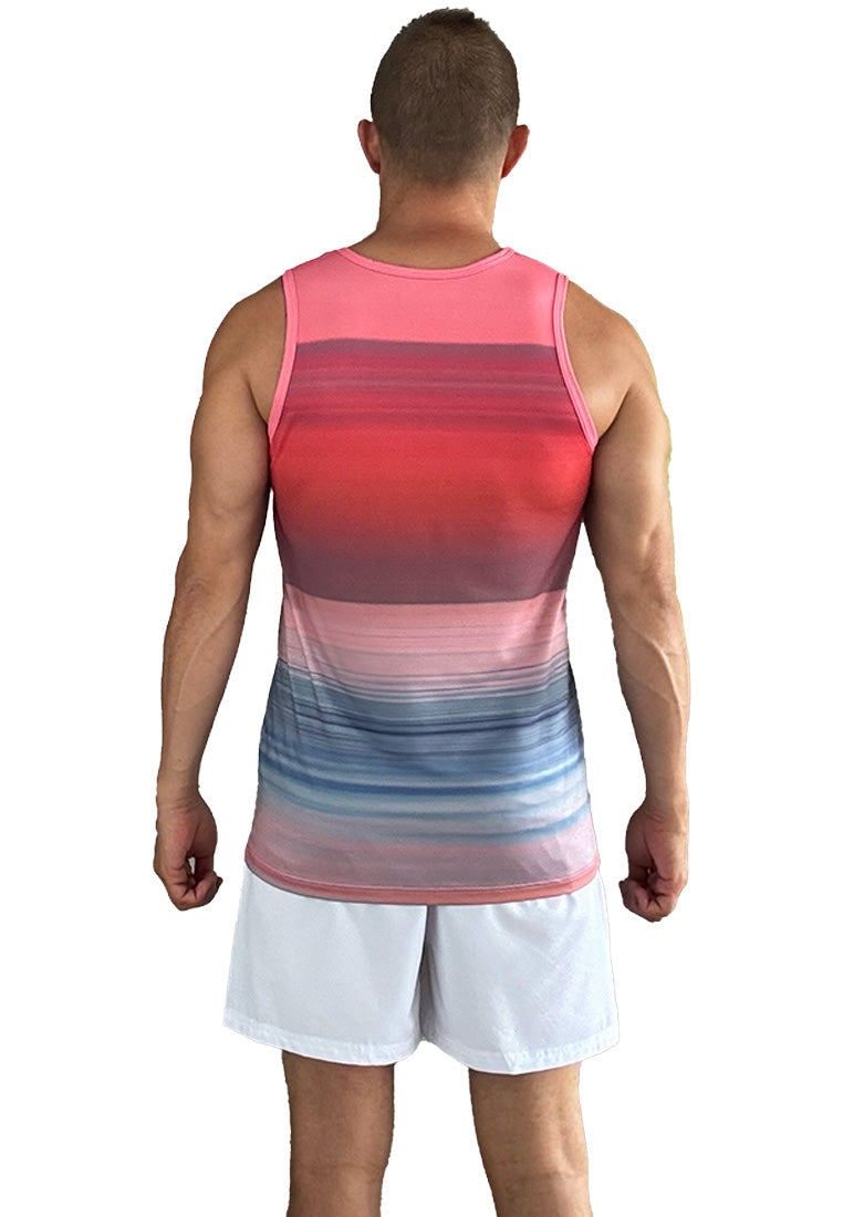 A man with short hair is standing facing away from the camera. He is wearing a Breathable Beach tank top "Sailboat" by BWET Swimwear with shades of pink, red, and blue in a gradient pattern, and minimalist white shorts.