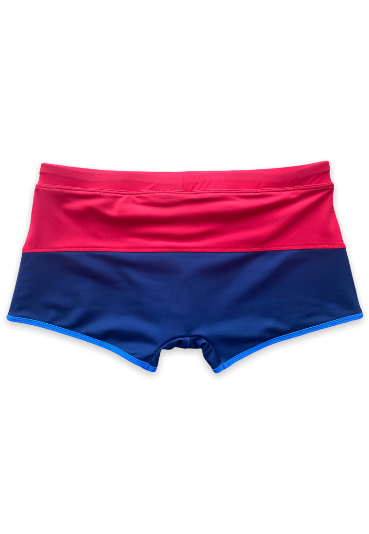 Introducing the Sentosa Beach Trunks by BWET Swimwear: high-quality and stylish swimwear featuring a bold color block design. With ultra-chlorine resistance and UV protection, these trunks boast a bright red upper section and a dark blue lower section, separated by a straight horizontal seam. Designed with a fitted, brief-like style, they promise both durability and cutting-edge fashion.